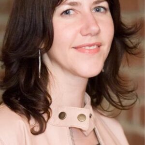 Portrait of a young woman with shoulder-length dark brown hair and blue eyes smiling gently indoors.