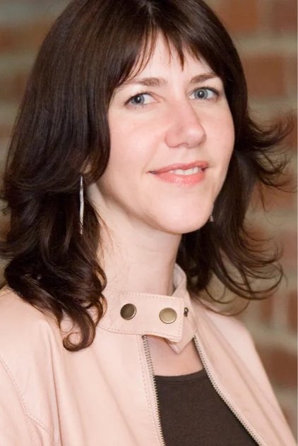 Portrait of a young woman with shoulder-length dark brown hair and blue eyes smiling gently indoors.